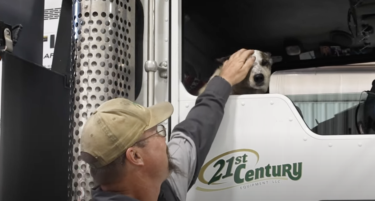 Technician Corey Munn next to his truck, petting his dog Ginger's head who is sitting in the passenger seat.